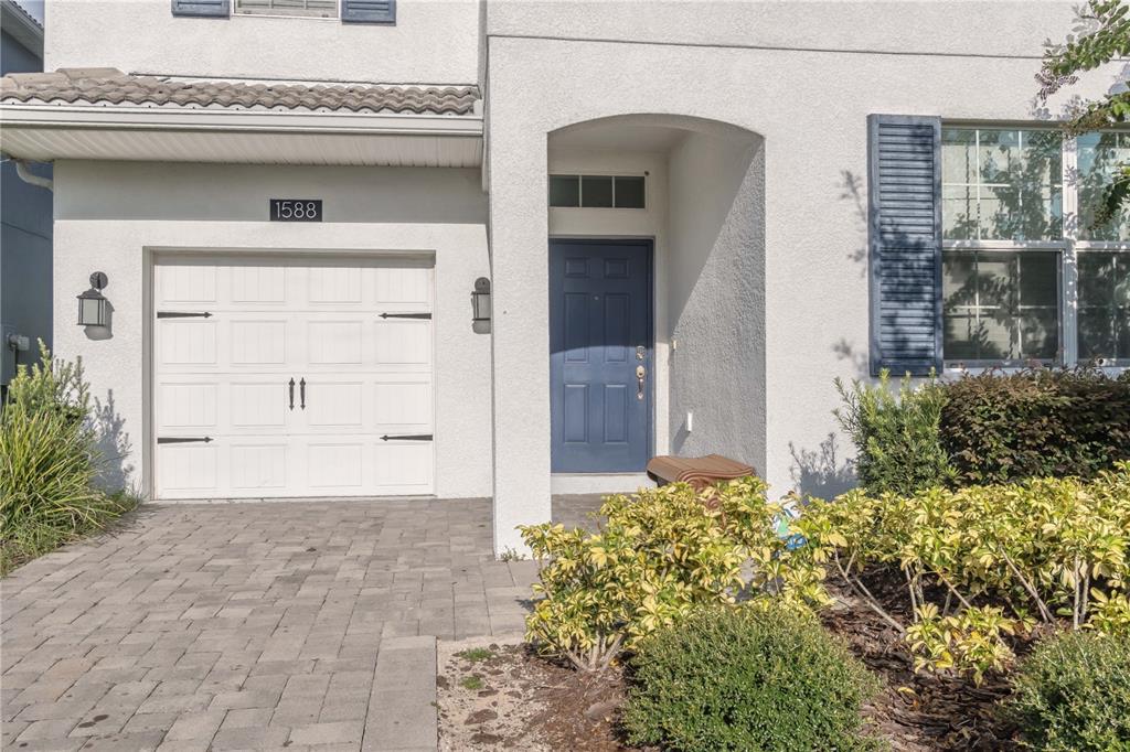 The exterior of a house features a white stucco facade, a blue front door, and a garage — 1588 FLANGE DRIVE, DAVENPORT, FL