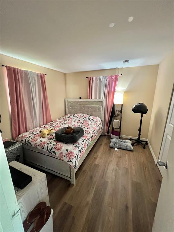 A bedroom features a bed with floral bedding, pink curtains, and wood-look flooring — 1701 MONTECITO AVENUE, DELTONA, FL