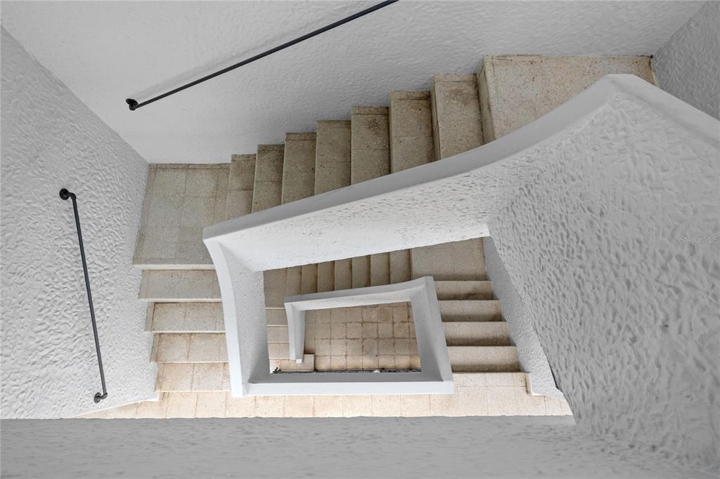 A high-angle view looking down a white, textured stairwell with stone steps and metal railings — 107 TAFT UNIT 5, SAN JUAN, PR