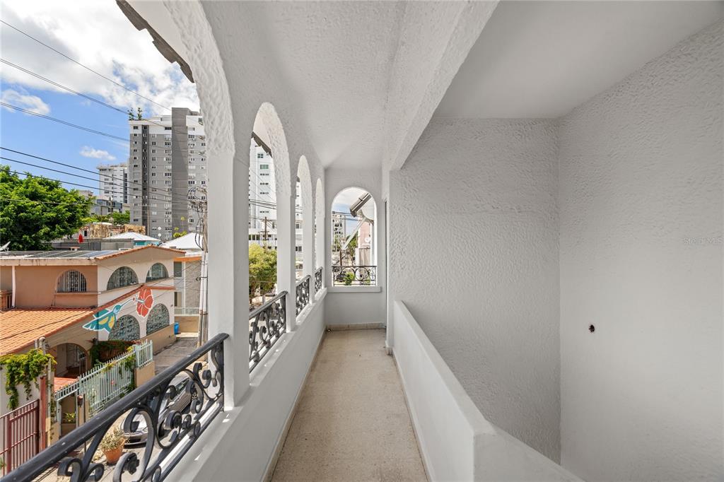 A white, covered balcony features arched openings, a black metal railing, and views of buildings — 107 TAFT UNIT 5, SAN JUAN, PR