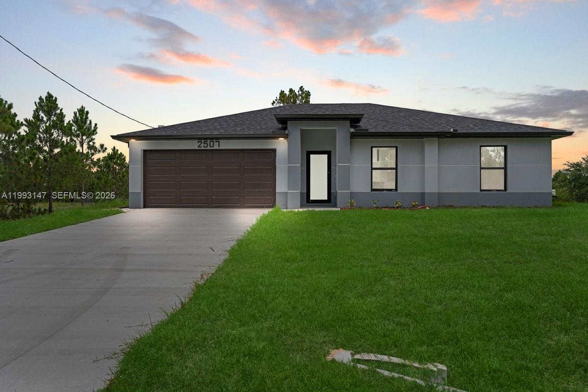 A modern gray single-story house features a dark garage door and a central entryway — 2507 E 15th ST, Lehigh Acres FL 33972, LEHIGH ACRES, FL