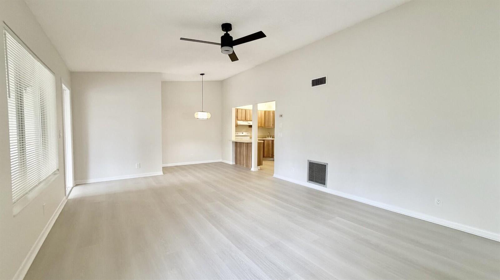 An empty living room features light wood-look flooring, a ceiling fan, and a kitchen pass-through — 4969 Sable Pine Circle # D2, West Palm Beach FL 33417, WEST PALM BEACH, FL