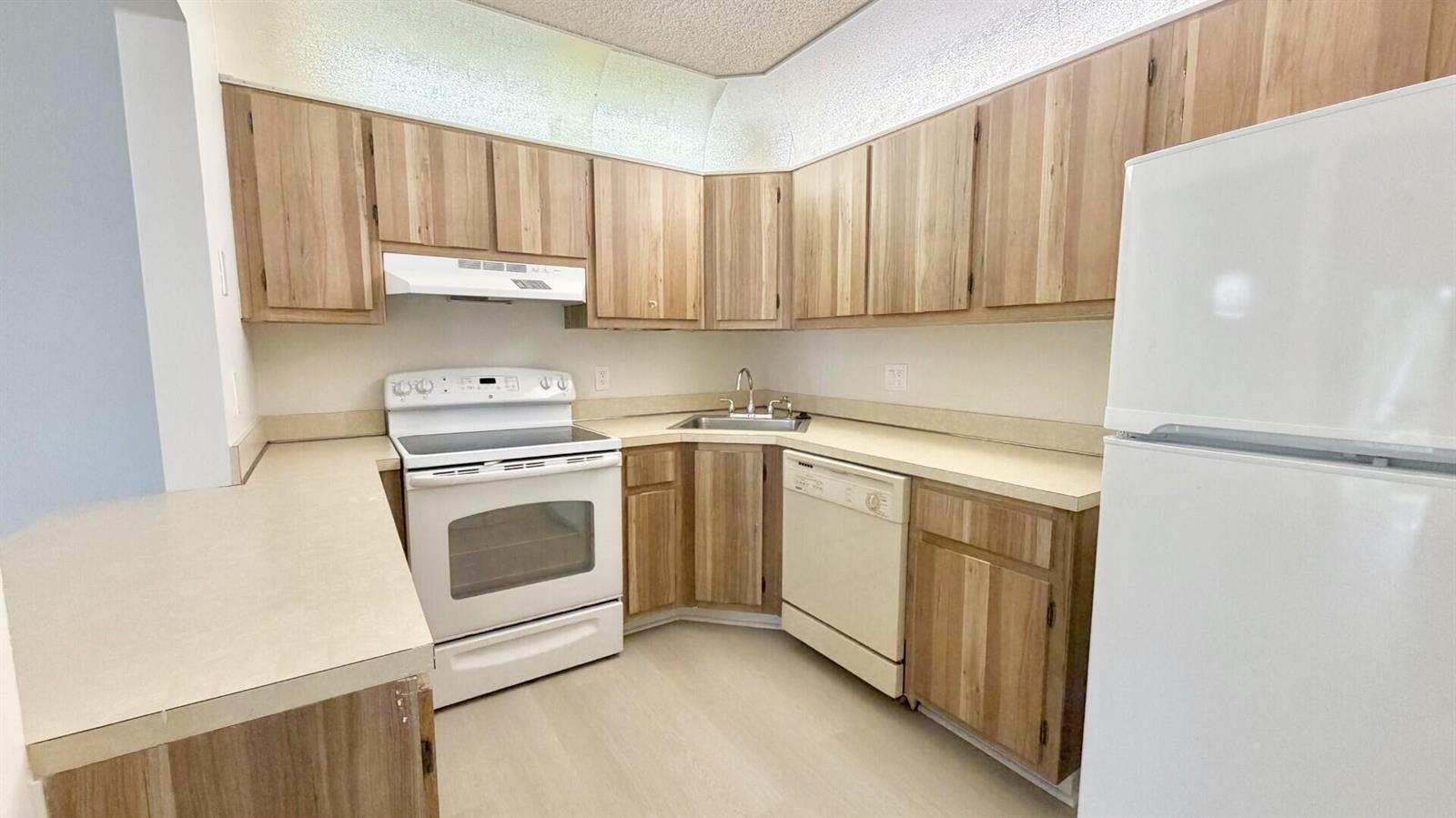 A kitchen features light wood cabinets, white appliances, a corner sink, and beige countertops — 4969 Sable Pine Circle # D2, West Palm Beach FL 33417, WEST PALM BEACH, FL