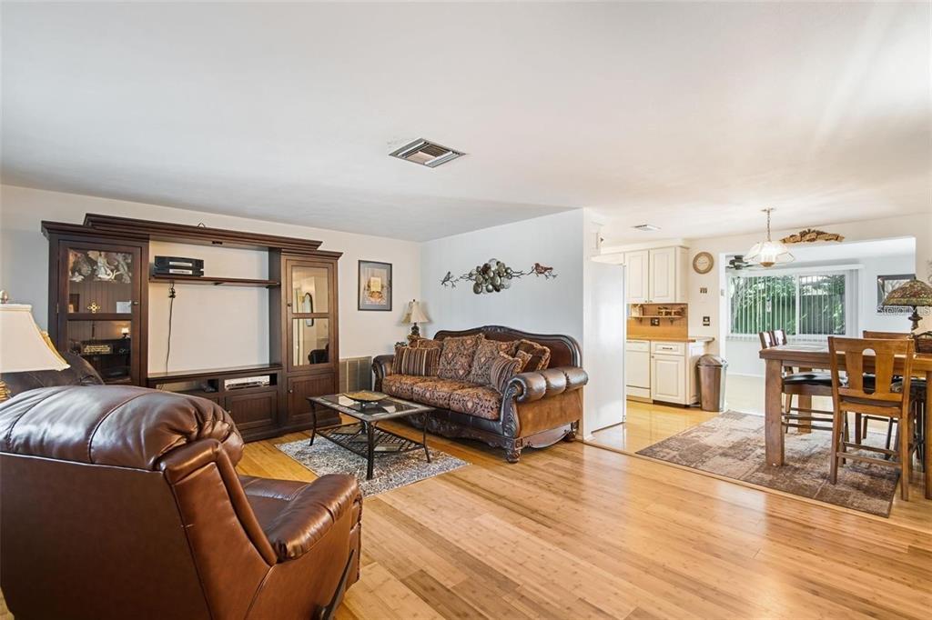 A living room with hardwood floors, a brown leather sofa, and an adjacent dining area — 3802 MYNABIRD DRIVE, NEW PORT RICHEY, FL