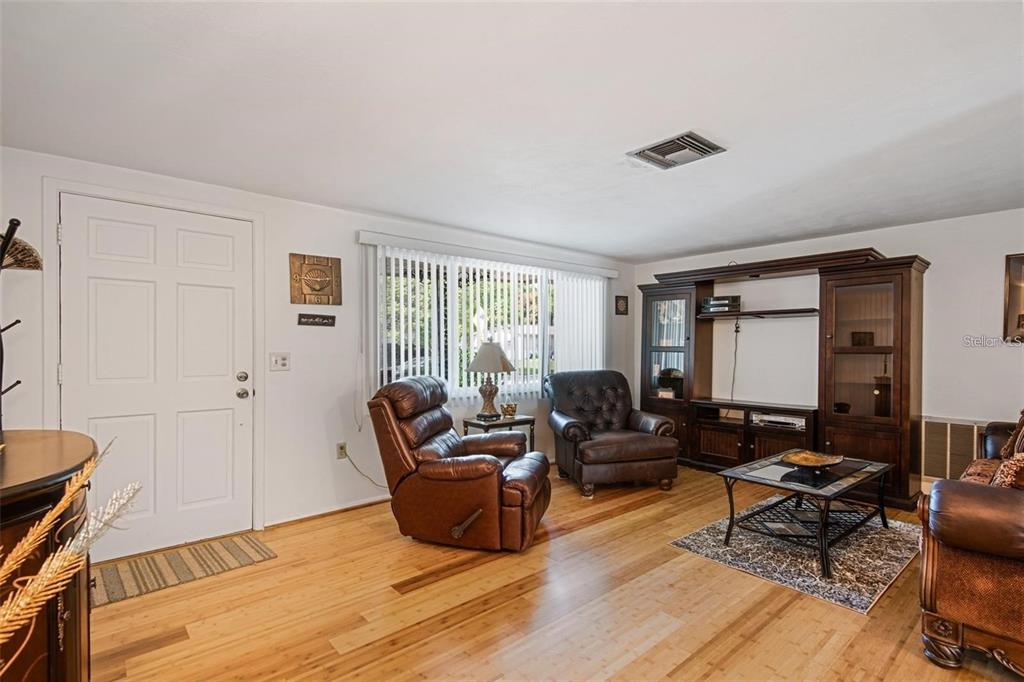 A living room with hardwood floors, leather furniture, a large entertainment center, and vertical blinds — 3802 MYNABIRD DRIVE, NEW PORT RICHEY, FL
