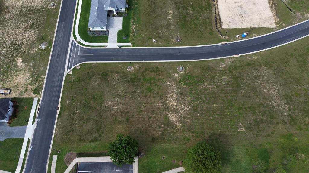 An aerial view shows a vacant residential lot situated at a curved street intersection — 229 SNOWY ORCHID WAY, LAKE ALFRED, FL