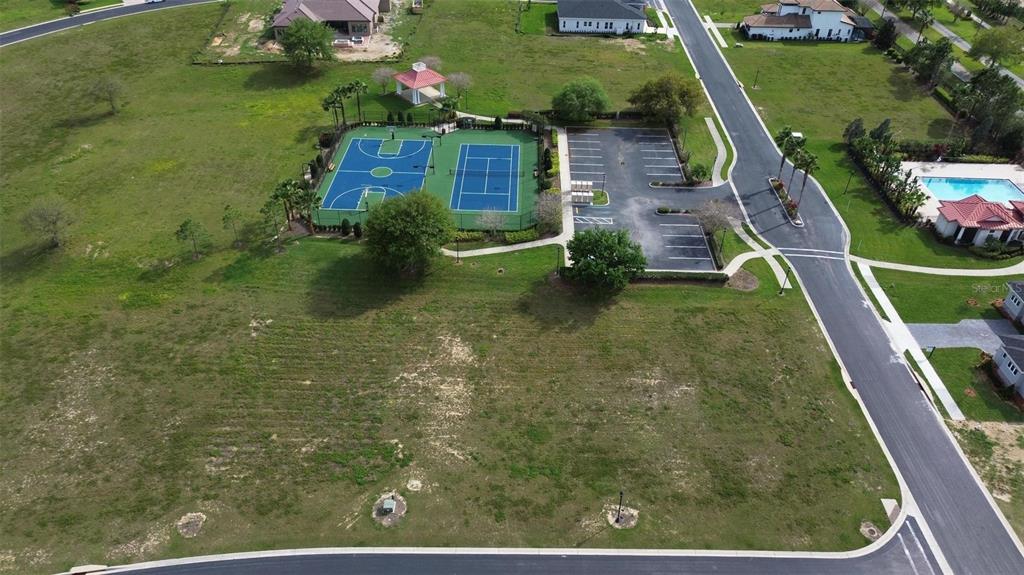 An aerial view shows a vacant residential lot next to a community sports court and parking — 229 SNOWY ORCHID WAY, LAKE ALFRED, FL