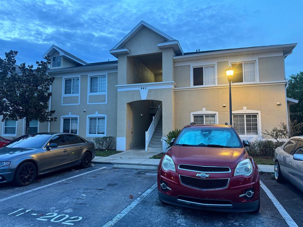 A two-story apartment building exterior features tan stucco walls and a central covered staircase — 6411 CYPRESSDALE DRIVE UNIT 202, RIVERVIEW, FL