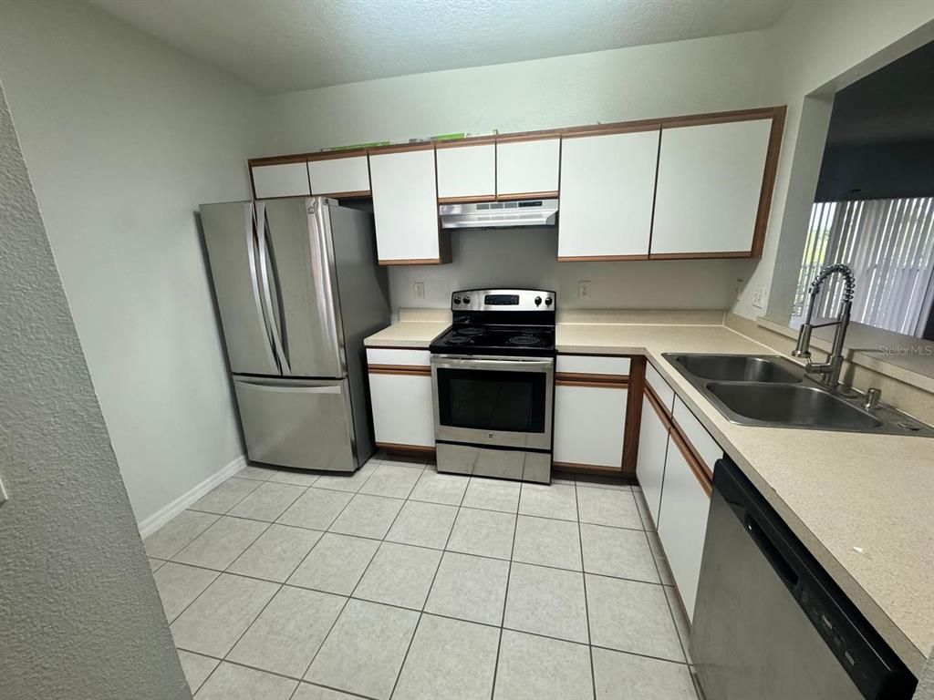 A kitchen features white cabinets, stainless steel appliances, a double sink, and tiled flooring — 6411 CYPRESSDALE DRIVE UNIT 202, RIVERVIEW, FL