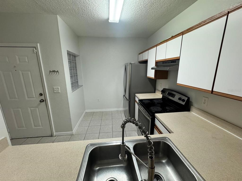 A kitchen features white cabinets, stainless steel appliances, a double sink, and tiled flooring — 6411 CYPRESSDALE DRIVE UNIT 202, RIVERVIEW, FL