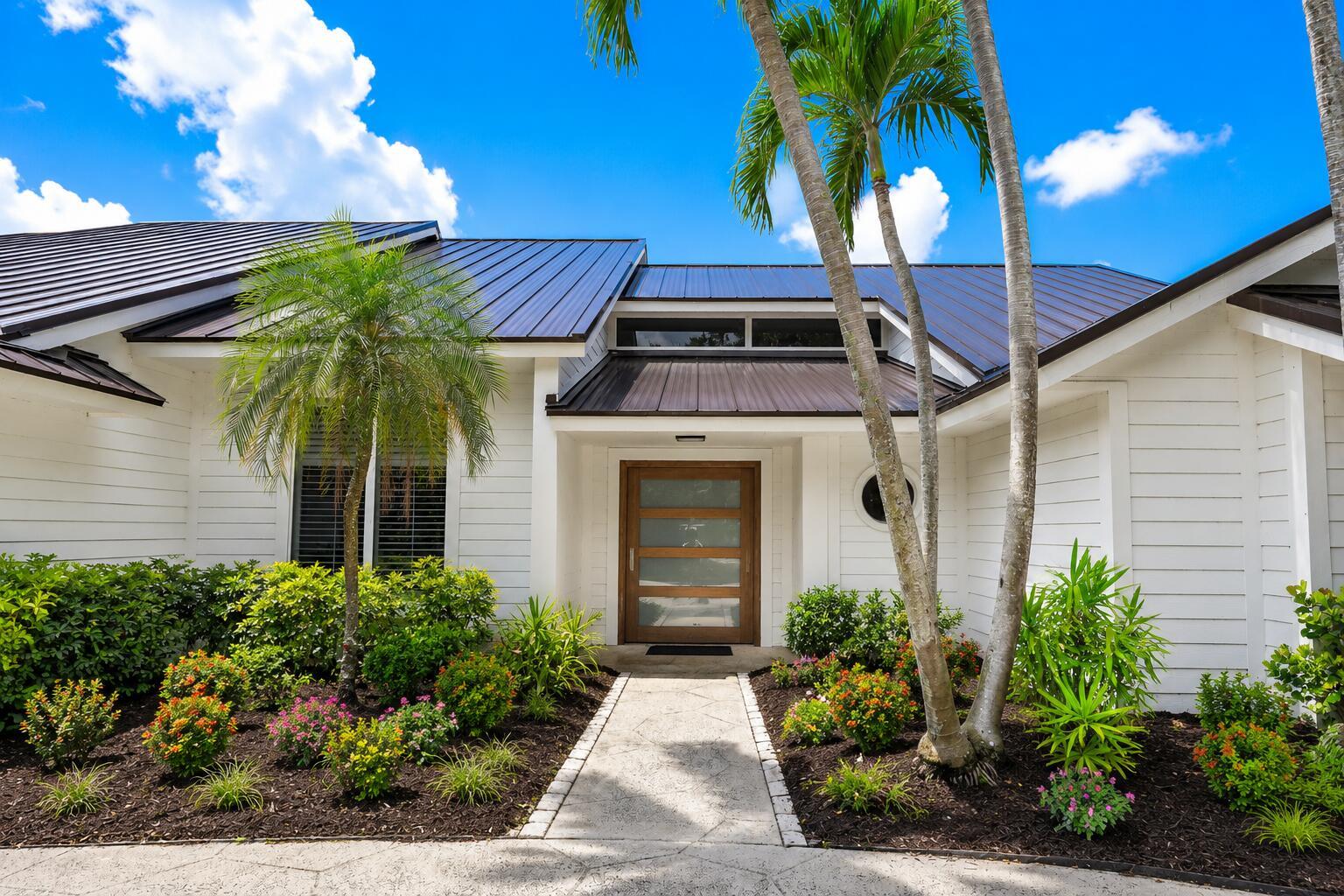 A white house with a metal roof, wooden front door, and palm trees in front — 10290 SE Banyan Way, Jupiter FL 33469, JUPITER, FL