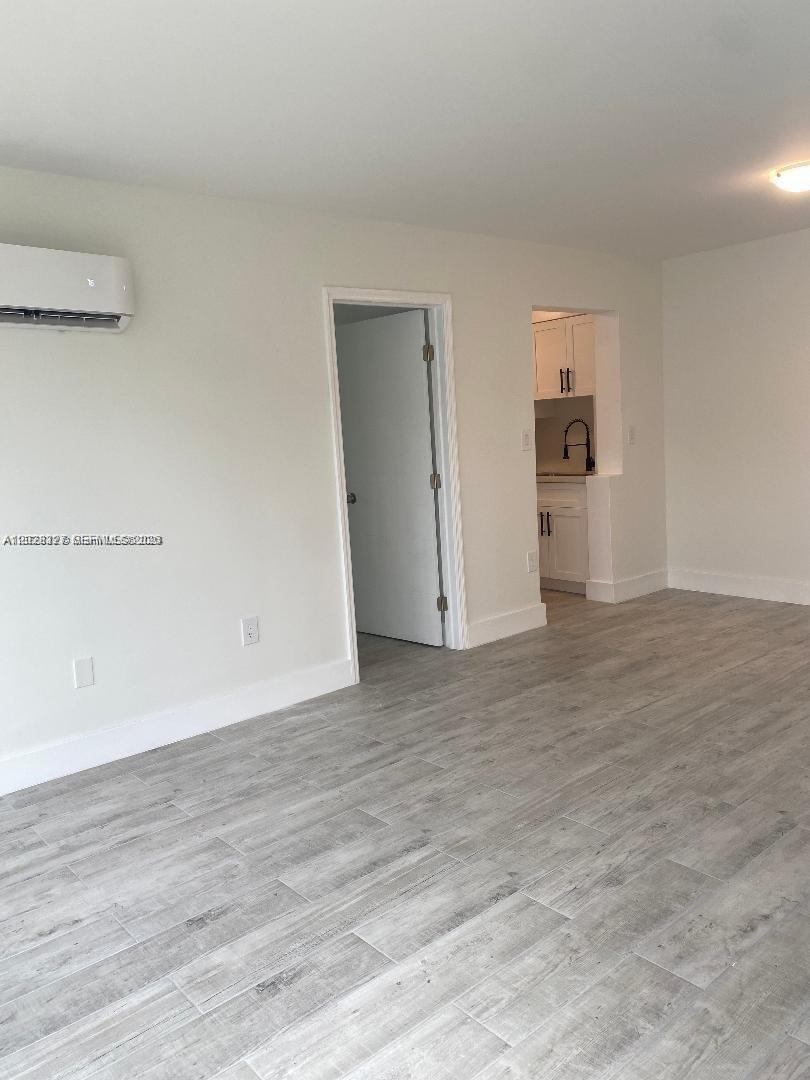 A room with light-colored wood-look tile flooring, a wall-mounted air conditioner, and a doorway — 2008 SW 3rd St # 1, Miami FL 33135, MIAMI, FL
