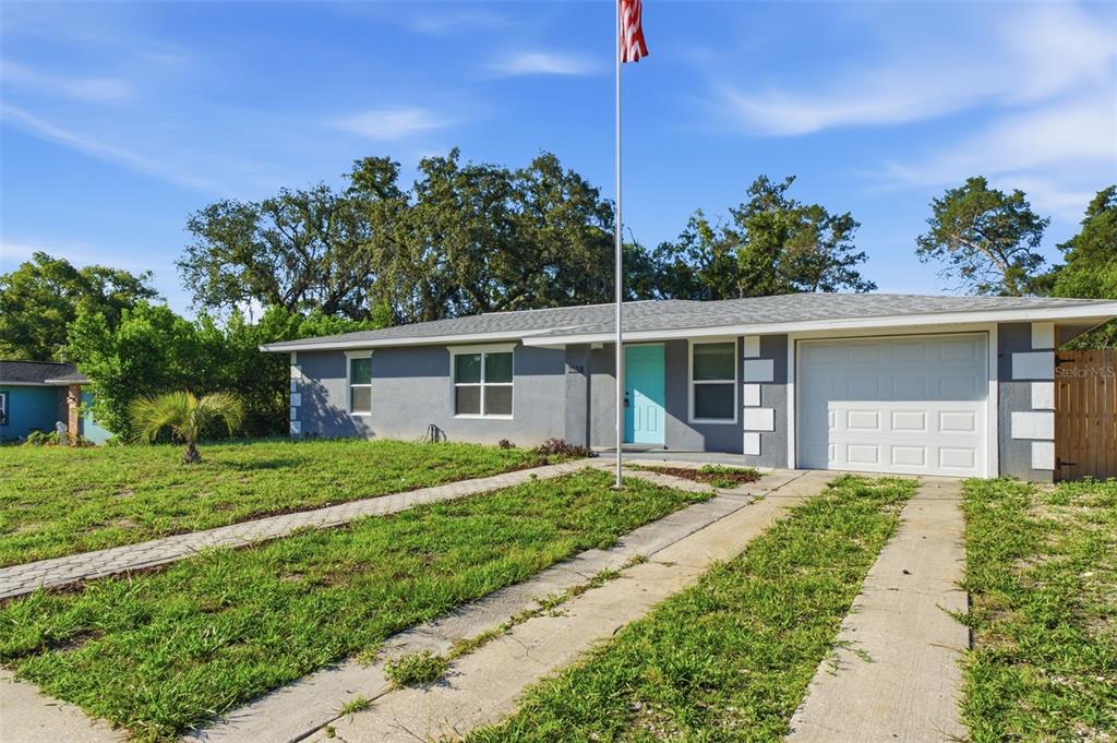 A single-story gray house with a white garage door and a light blue front door — 7178 HOLIDAY DRIVE, SPRING HILL, FL