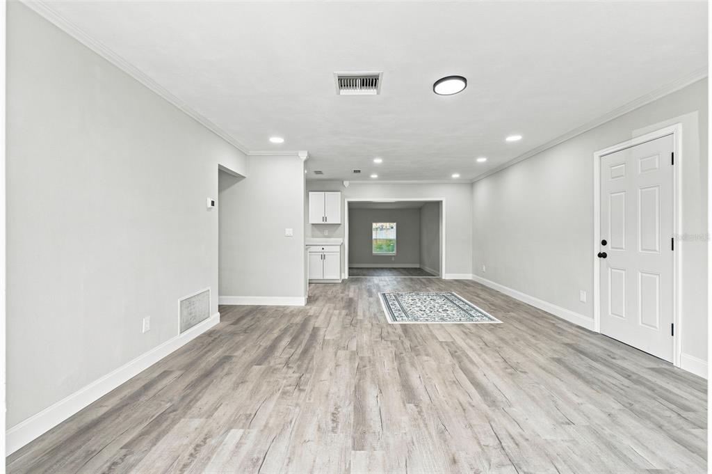 A living area with light gray walls, wood-look flooring, and a doorway to a kitchen — 7178 HOLIDAY DRIVE, SPRING HILL, FL