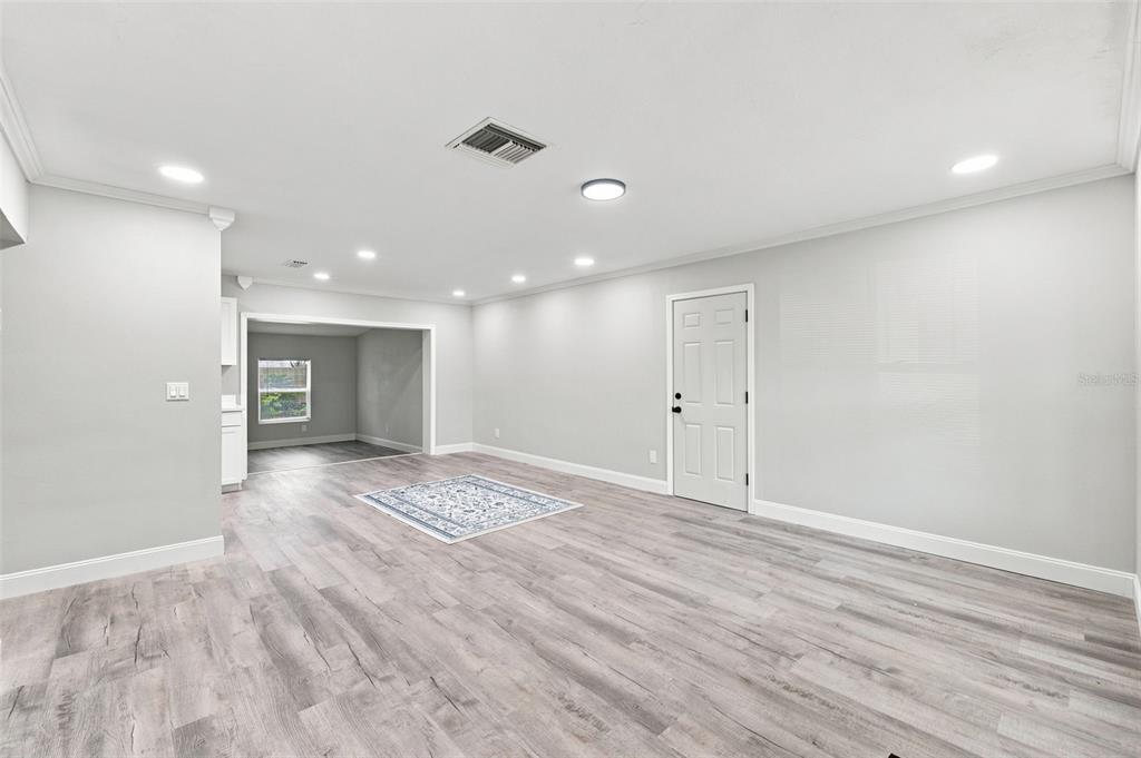 A spacious room features light gray walls, wood-look flooring, recessed lighting, and a white door — 7178 HOLIDAY DRIVE, SPRING HILL, FL