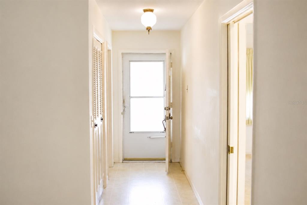 A hallway with light-colored walls, tile flooring, a ceiling light, and a white exterior door — 1656 S LAKE AVENUE UNIT 4, CLEARWATER, FL