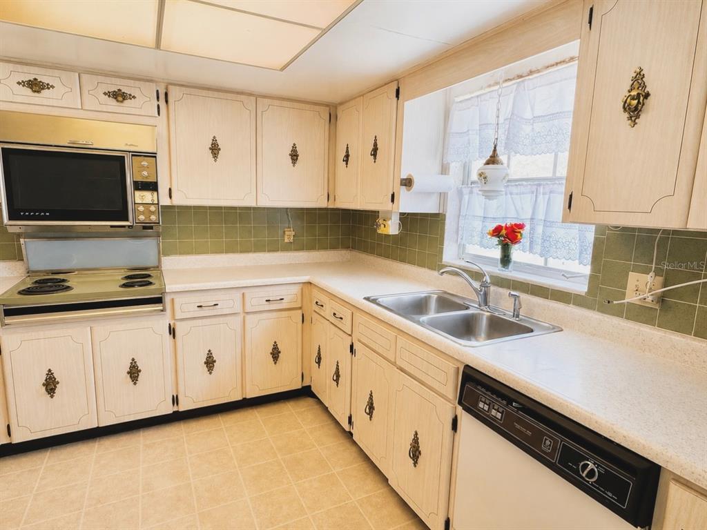 A kitchen features off-white cabinets, green tile backsplash, laminate countertops, and a double-basin sink — 1656 S LAKE AVENUE UNIT 4, CLEARWATER, FL