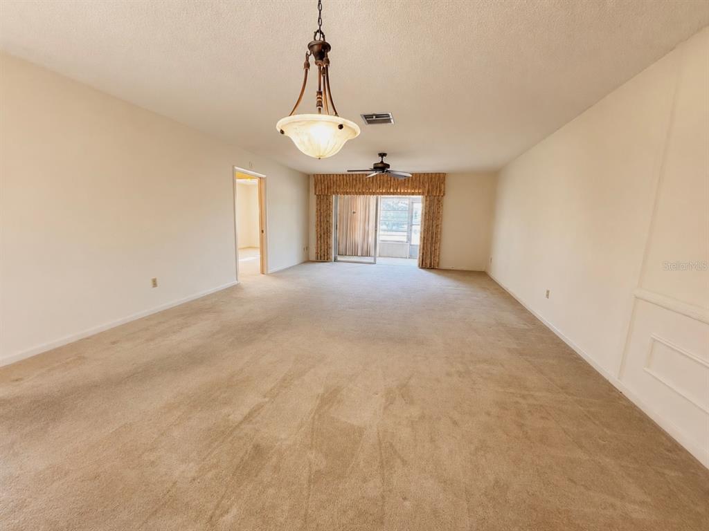 A spacious living room features beige carpeting, a ceiling fan, and a hanging light fixture — 1656 S LAKE AVENUE UNIT 4, CLEARWATER, FL