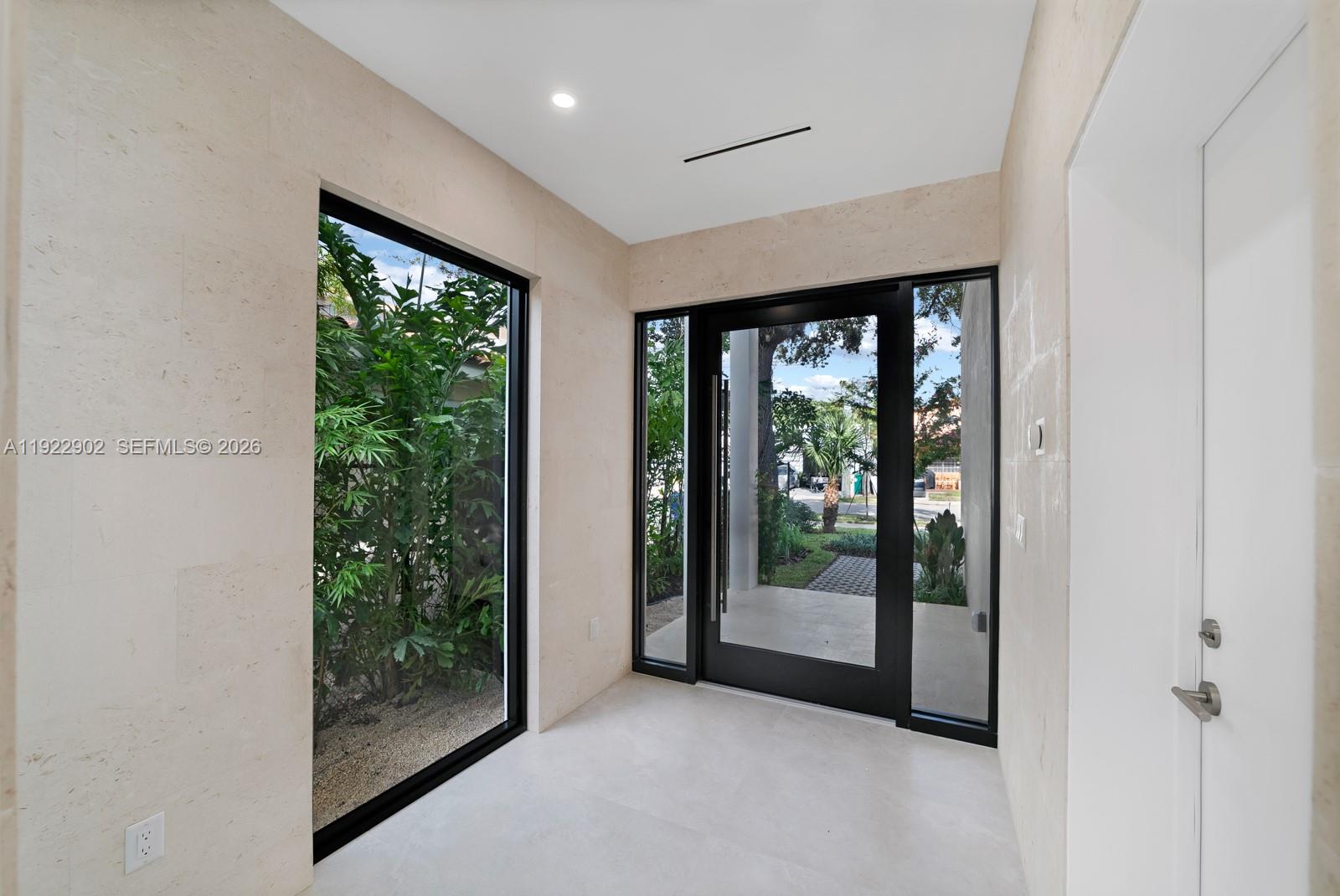 A modern entryway features light stone walls, large glass windows, and a black-framed front door — 2610 SW 17th St, Miami FL 33145, MIAMI, FL