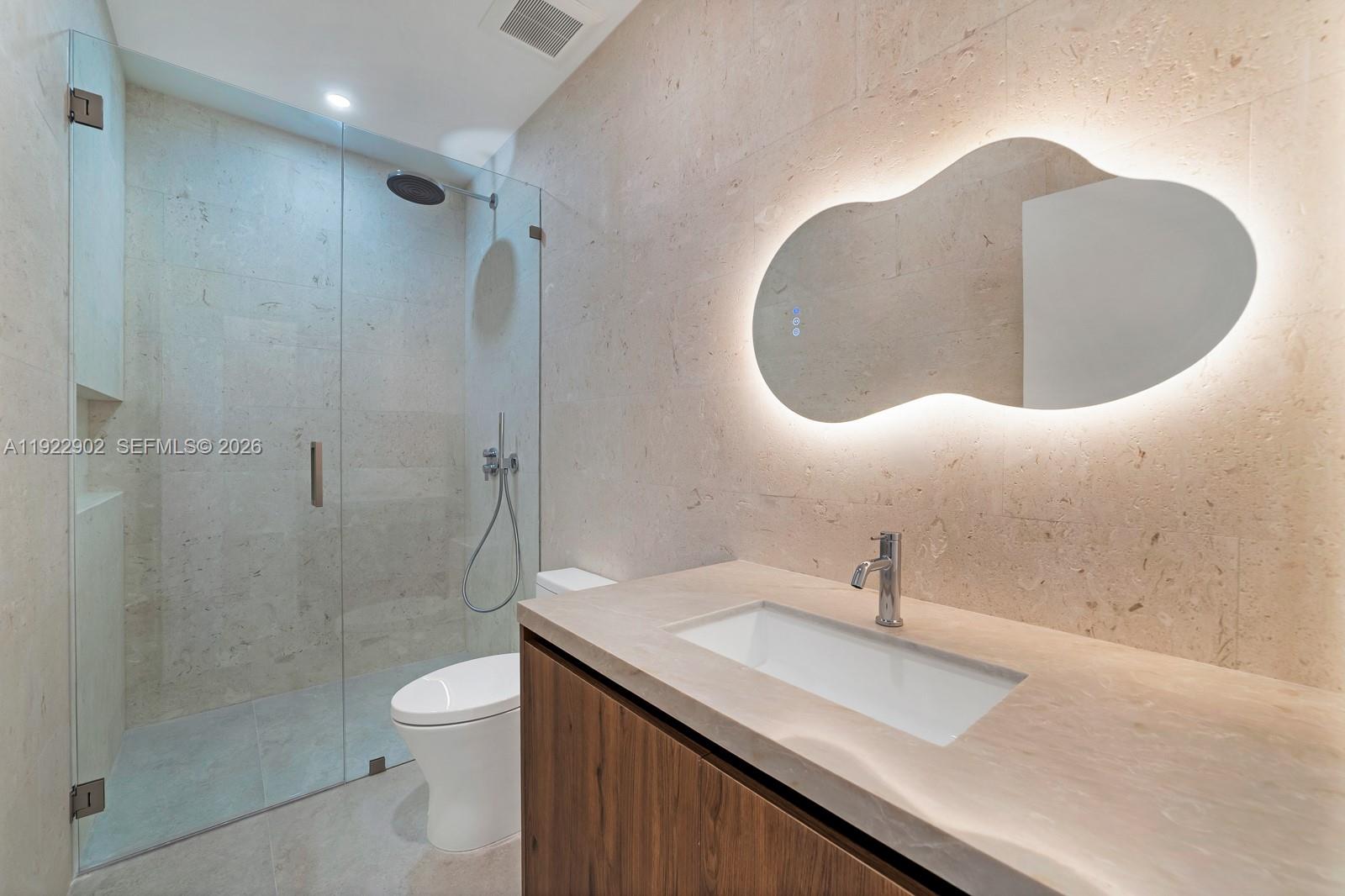 A modern bathroom features a floating wood vanity, stone countertop, and an organic-shaped LED mirror — 2610 SW 17th St, Miami FL 33145, MIAMI, FL