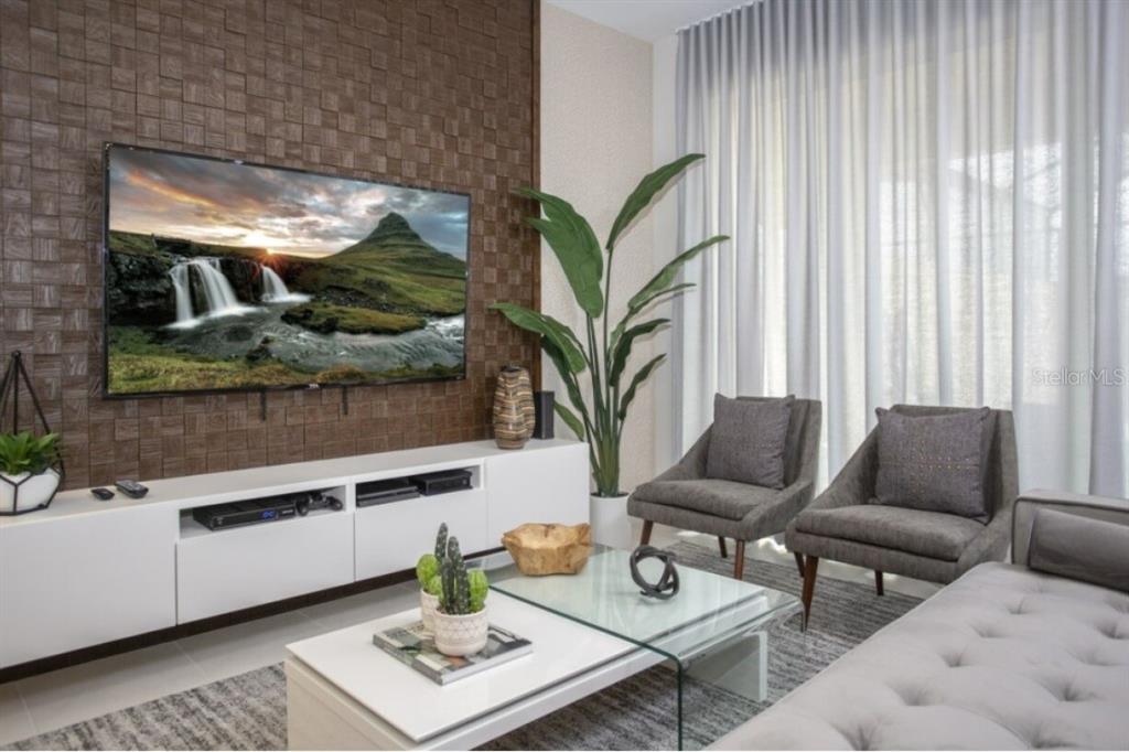 A modern living room features a textured wood accent wall, a television, and two armchairs — 1561 CAREY PALM CIRCLE, KISSIMMEE, FL
