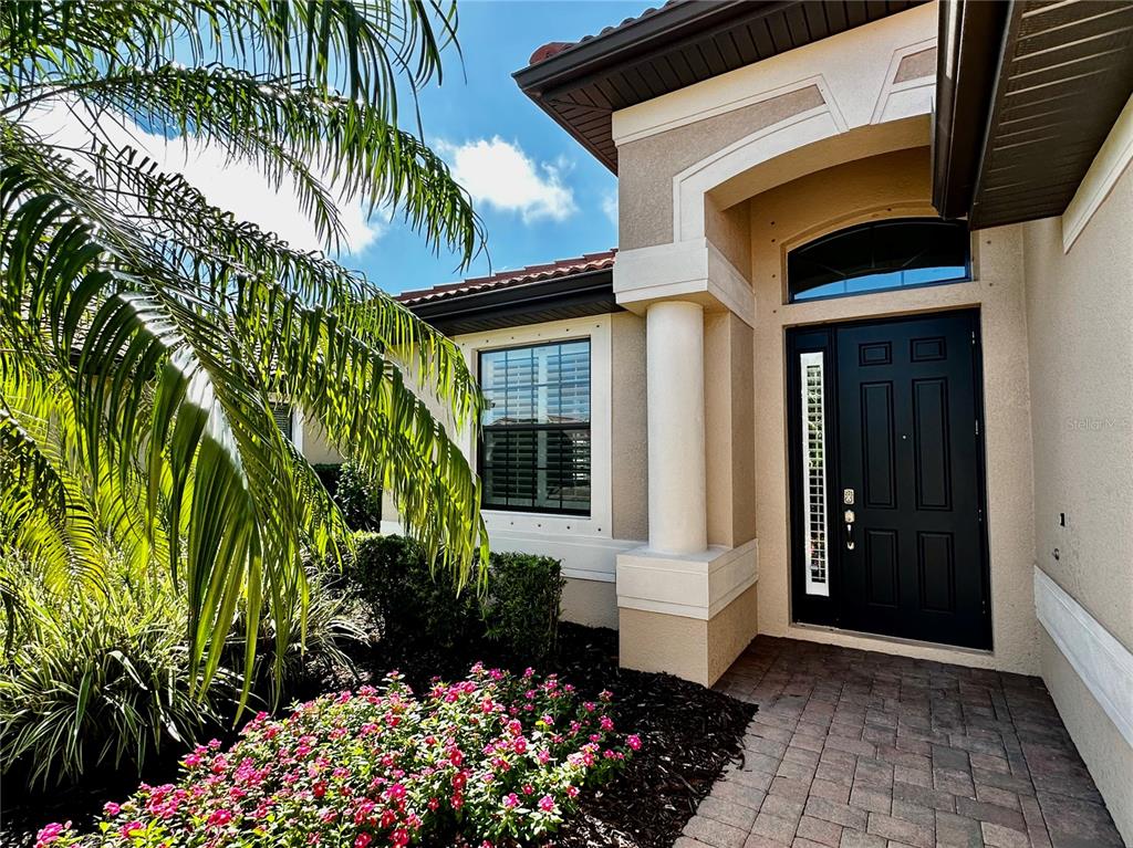 The front entrance features a dark door with a sidelight, a column, and landscaping — 1321 CIELO COURT, NOKOMIS, FL
