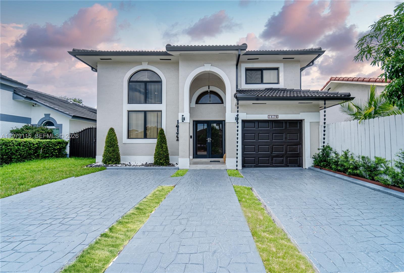 A two-story house features a gray paved driveway, a dark garage door, and arched windows — 14172 NW 87th Ct, Miami Lakes FL 33018, MIAMI LAKES, FL