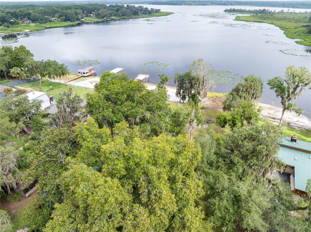 An aerial view shows a lakefront property with trees, a sandy shoreline, and several docks — 114 LITTLE ORANGE LAKE DRIVE, HAWTHORNE, FL