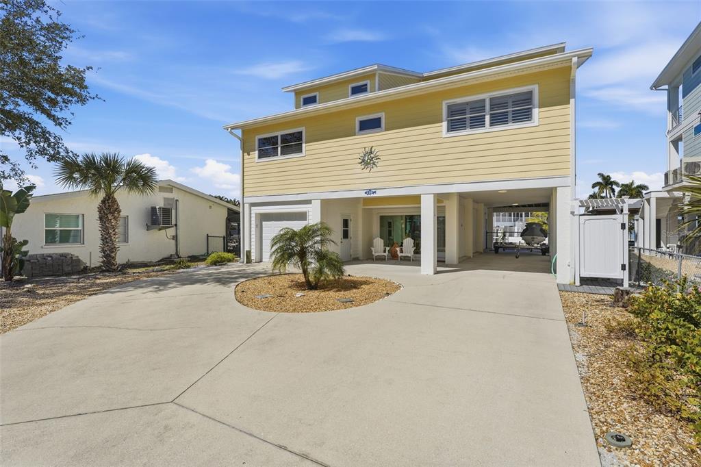 A yellow two-story house with a concrete driveway and a covered ground-level parking area — 220 MOCKINGBIRD STREET, ENGLEWOOD, FL