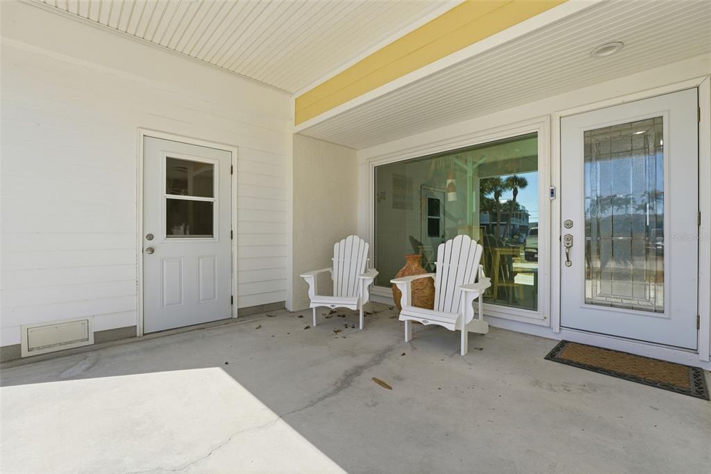 A covered concrete patio features two white Adirondack chairs, a glass door, and a side door — 220 MOCKINGBIRD STREET, ENGLEWOOD, FL