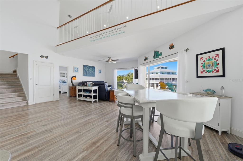 A bright living and dining area with vaulted ceilings, wood-look flooring, and a balcony view — 220 MOCKINGBIRD STREET, ENGLEWOOD, FL