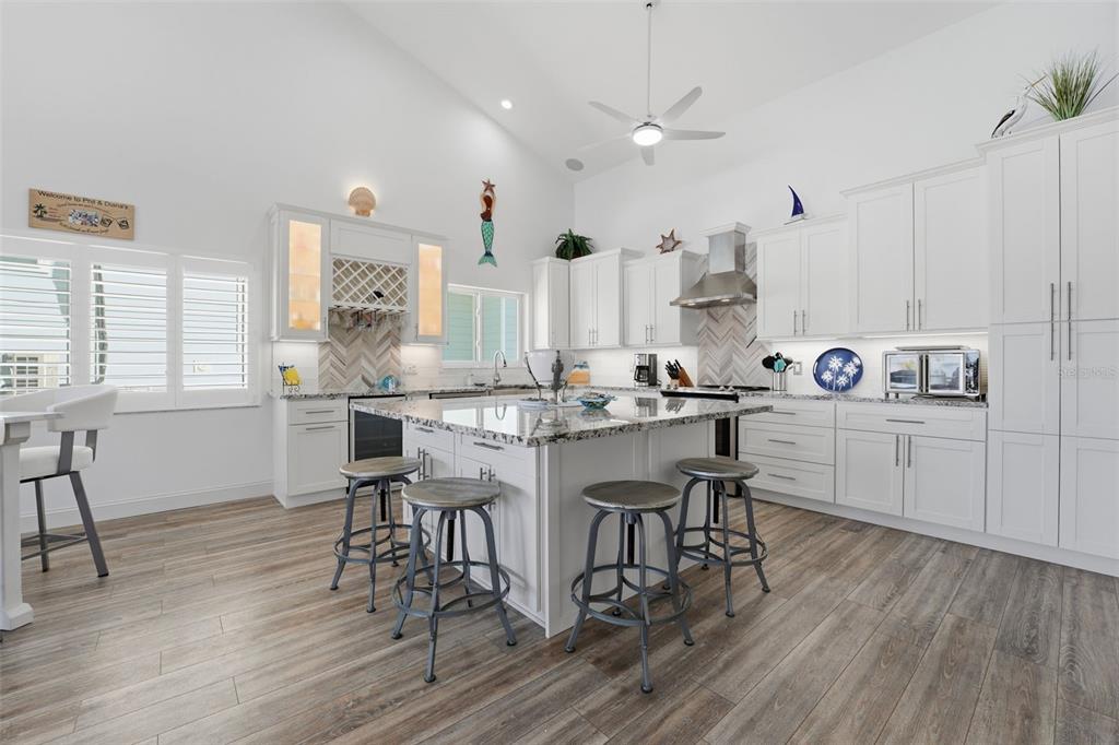 A bright kitchen features white cabinetry, a large granite island with stools, and wood-look flooring — 220 MOCKINGBIRD STREET, ENGLEWOOD, FL