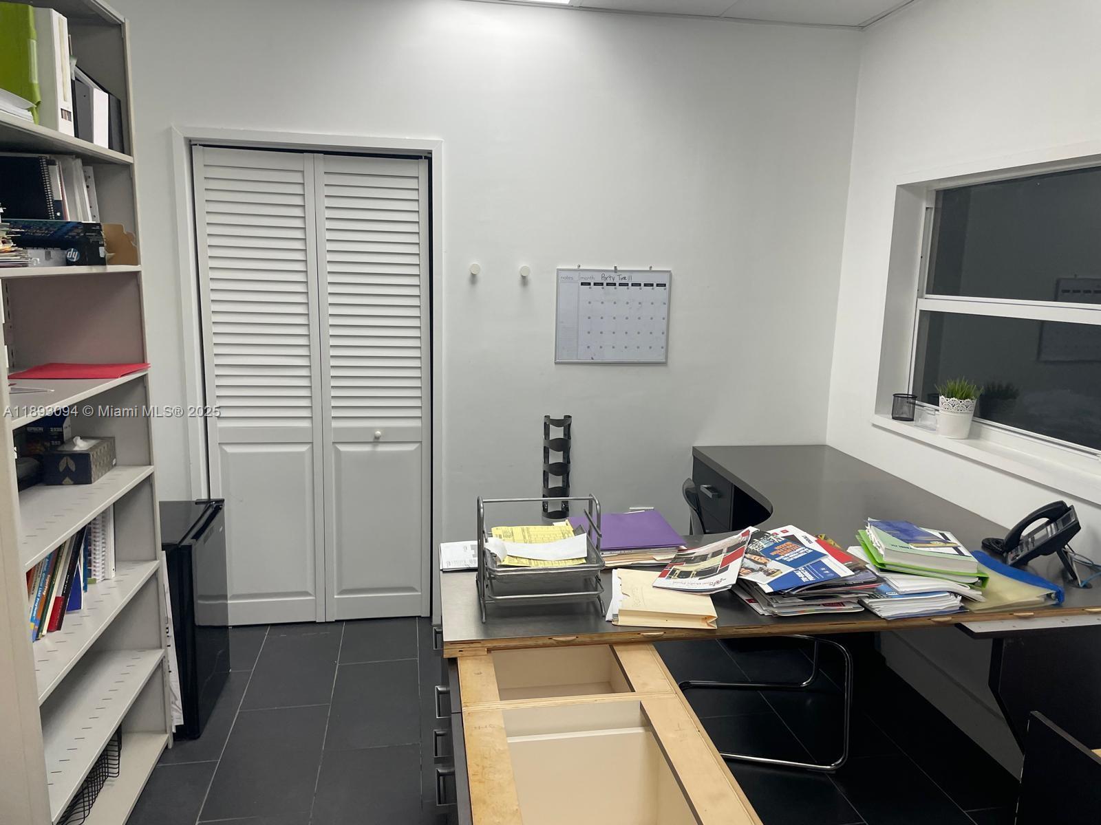 A home office features a desk, shelving unit, white louvered closet doors, and tiled flooring — 10820 NW 138th St # C, Hialeah Gardens FL 33018, HIALEAH GARDENS, FL