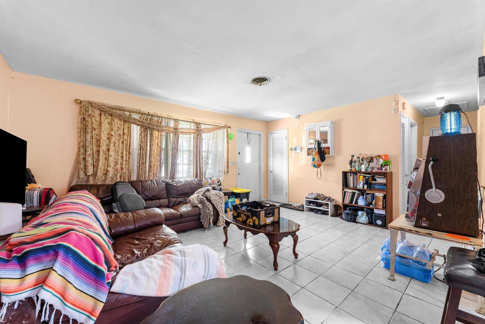 A living room with light-colored tile floors, peach walls, a brown leather sofa, and curtains — 2106 WARE Drive, West Palm Beach FL 33409, WEST PALM BEACH, FL