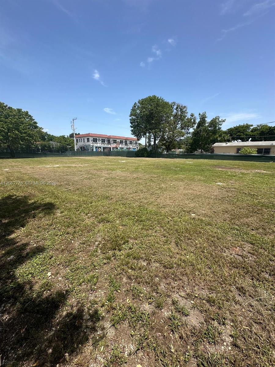 A large, flat, grassy vacant lot is enclosed by a green fence under a blue sky — 3311 NW 2nd Ave, Miami FL 33127, MIAMI, FL