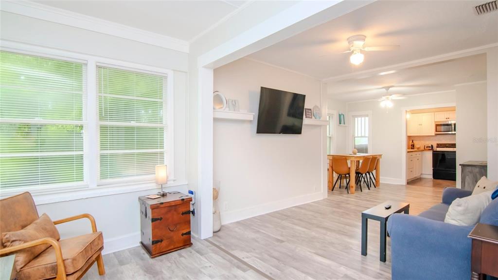 A bright living room with light wood-look flooring flows into a dining area and kitchen — 1466 LAURA STREET, CLEARWATER, FL
