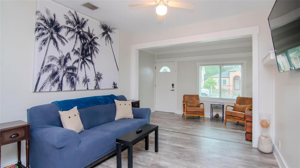 A living room features a blue sofa, two leather chairs, and a large palm tree print — 1466 LAURA STREET, CLEARWATER, FL