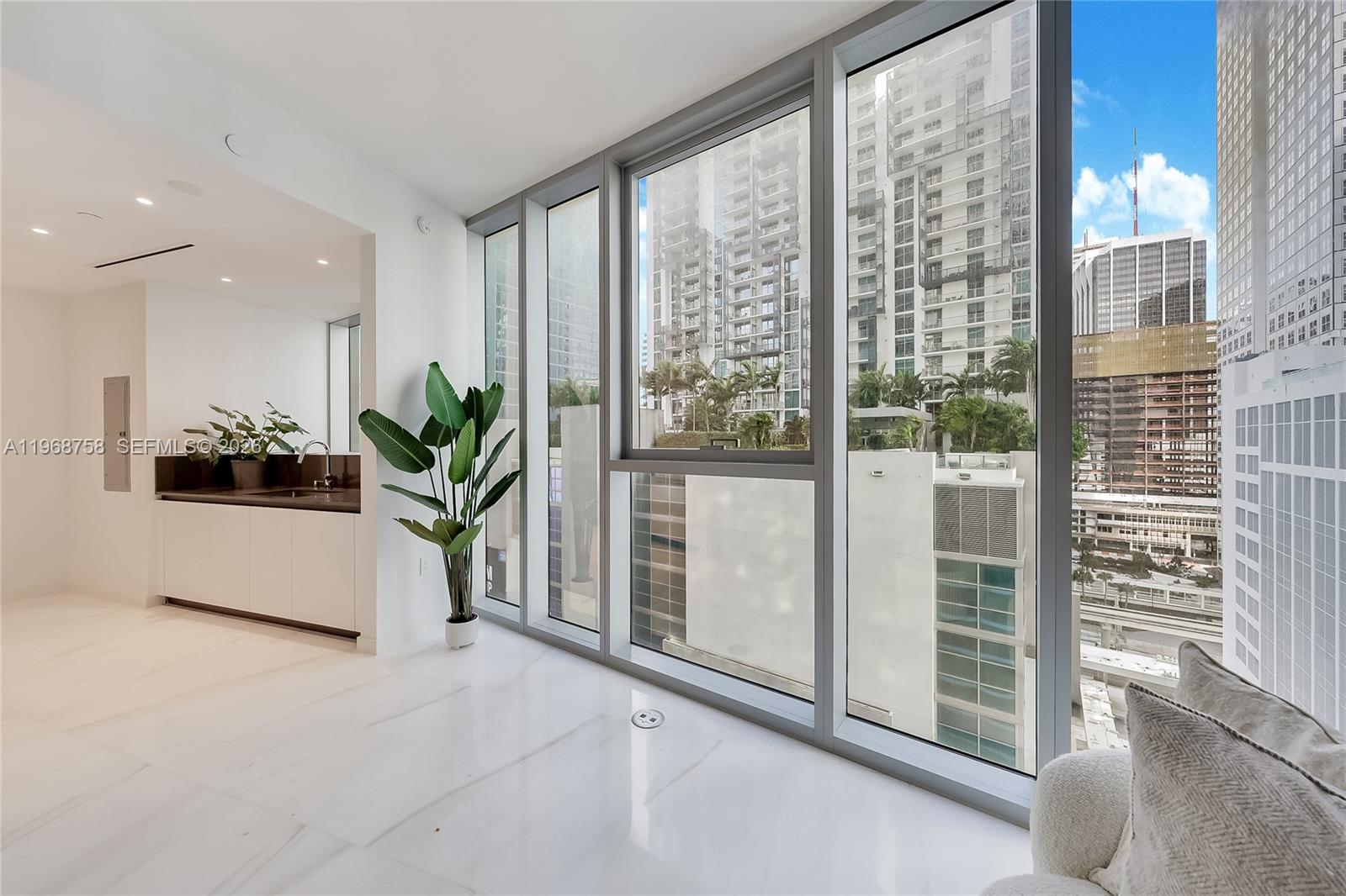 A modern room with white marble floors, a small kitchenette, and floor-to-ceiling windows overlooking buildings — 300 Biscayne Boulevard Way # 1105C, Miami FL 33131, MIAMI, FL