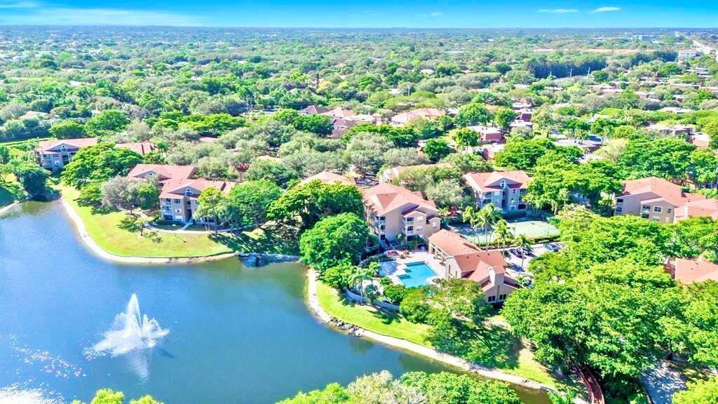An aerial view of a multi-story apartment complex with a lake, fountain, and swimming pool — 1745 Palm Cove Boulevard # 209, Delray Beach FL 33445, DELRAY BEACH, FL