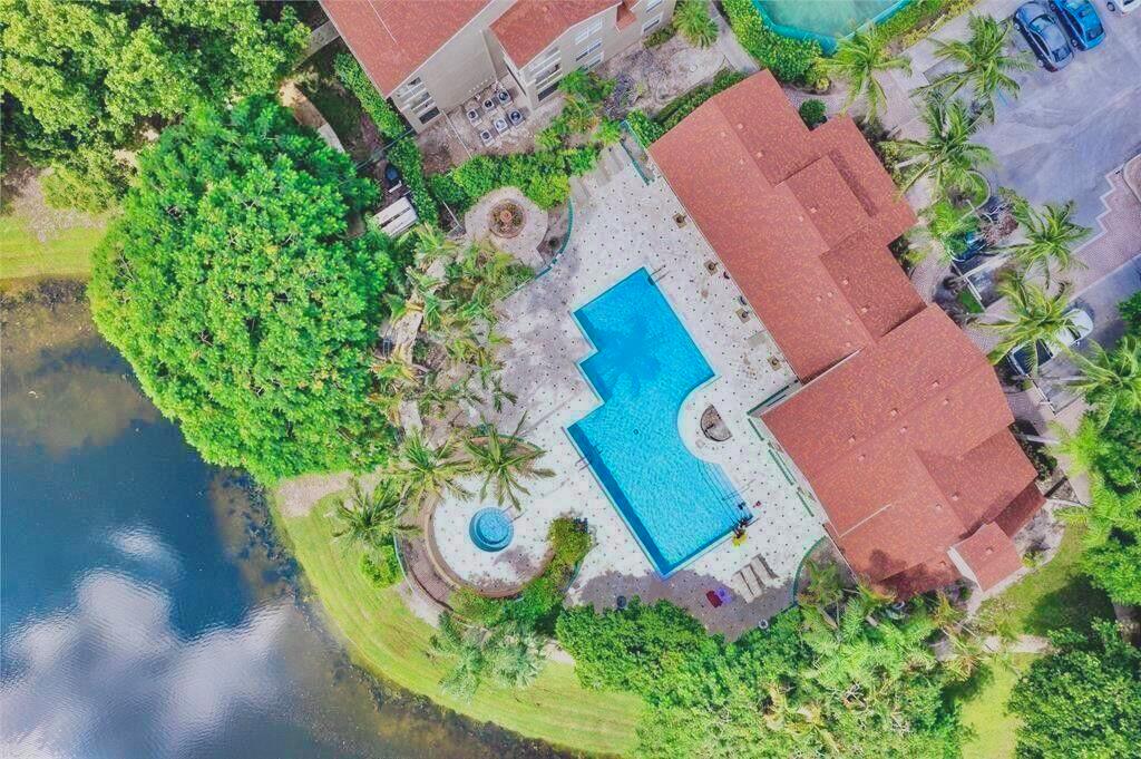 An aerial view shows a swimming pool and patio area next to a building and lake — 1745 Palm Cove Boulevard # 209, Delray Beach FL 33445, DELRAY BEACH, FL
