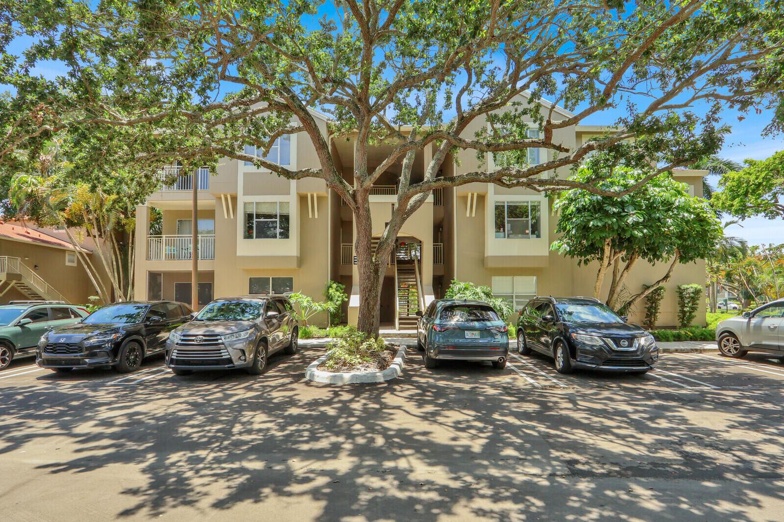 A three-story apartment building with a large tree in front of a parking lot — 1745 Palm Cove Boulevard # 209, Delray Beach FL 33445, DELRAY BEACH, FL