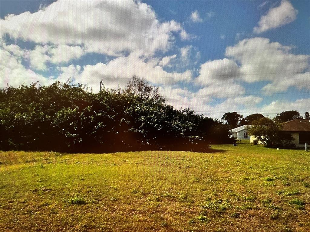 A grassy, vacant lot features a large, dense hedge and a neighboring house in the distance — LOT#27 SAN MARCO AVENUE, NORTH PORT, FL