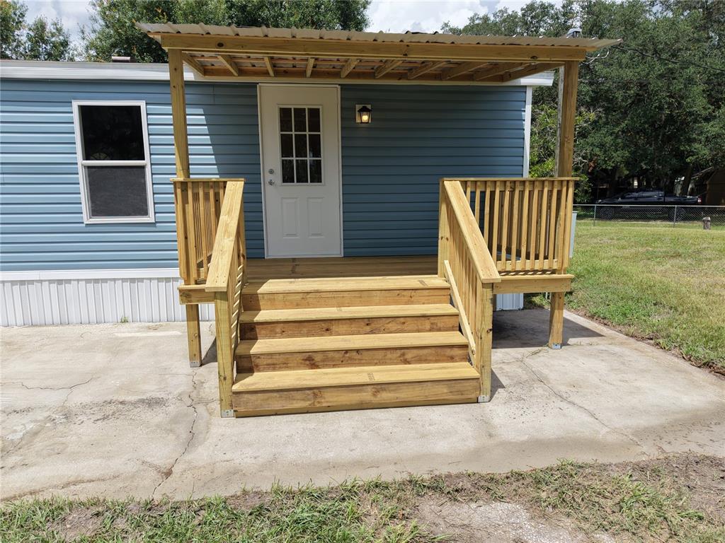 A blue mobile home features a new wooden deck with stairs and a metal roof — 18577 EVERETT RD, ORLANDO, FL