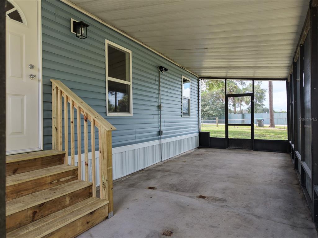 A covered concrete patio with wooden stairs leading to a blue-sided home with screened walls — 18577 EVERETT RD, ORLANDO, FL