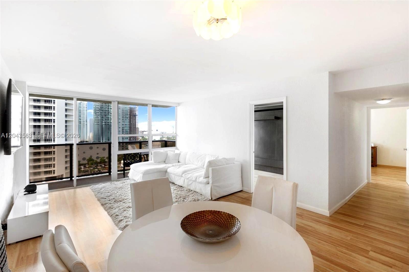 A bright living and dining area features white furniture, light wood floors, and floor-to-ceiling windows — 600 NE 36th St # 1717, Miami FL 33137, MIAMI, FL