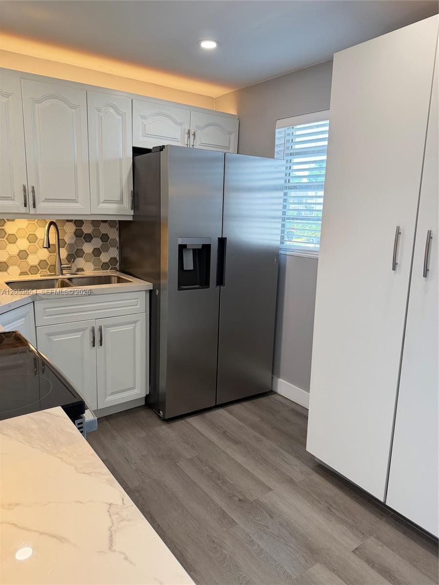 A kitchen features white cabinets, stainless steel appliances, a hexagonal backsplash, and wood-look flooring — 14185 SW 87th St # 212A, Miami FL 33183, MIAMI, FL