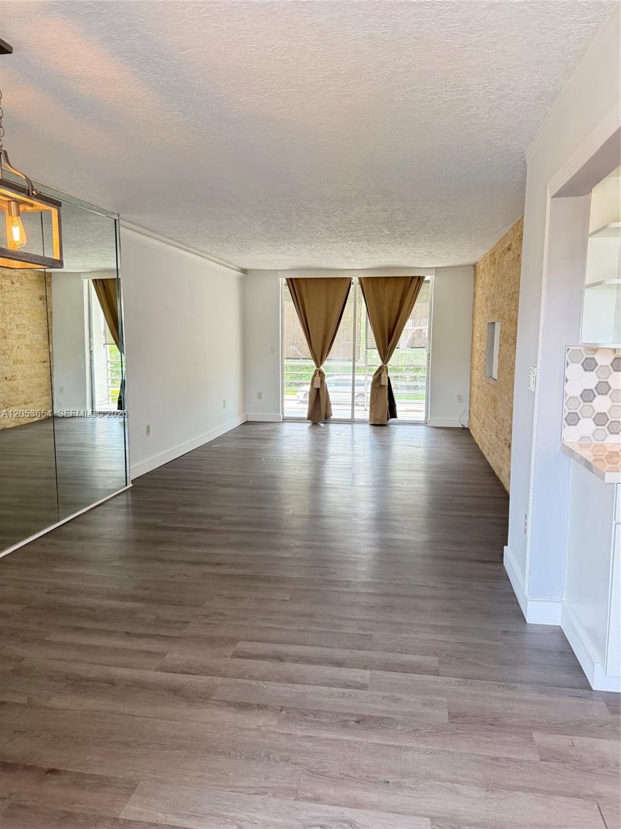 A living room features wood-look flooring, a mirrored wall, and a textured stone accent wall — 14185 SW 87th St # 212A, Miami FL 33183, MIAMI, FL