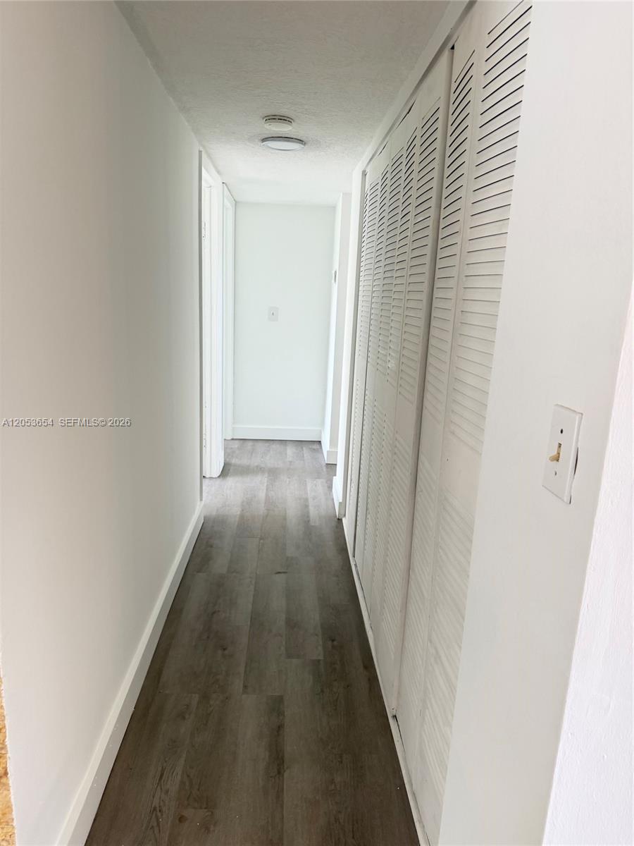 A narrow hallway features light-colored walls, wood-look flooring, and white louvered closet doors — 14185 SW 87th St # 212A, Miami FL 33183, MIAMI, FL