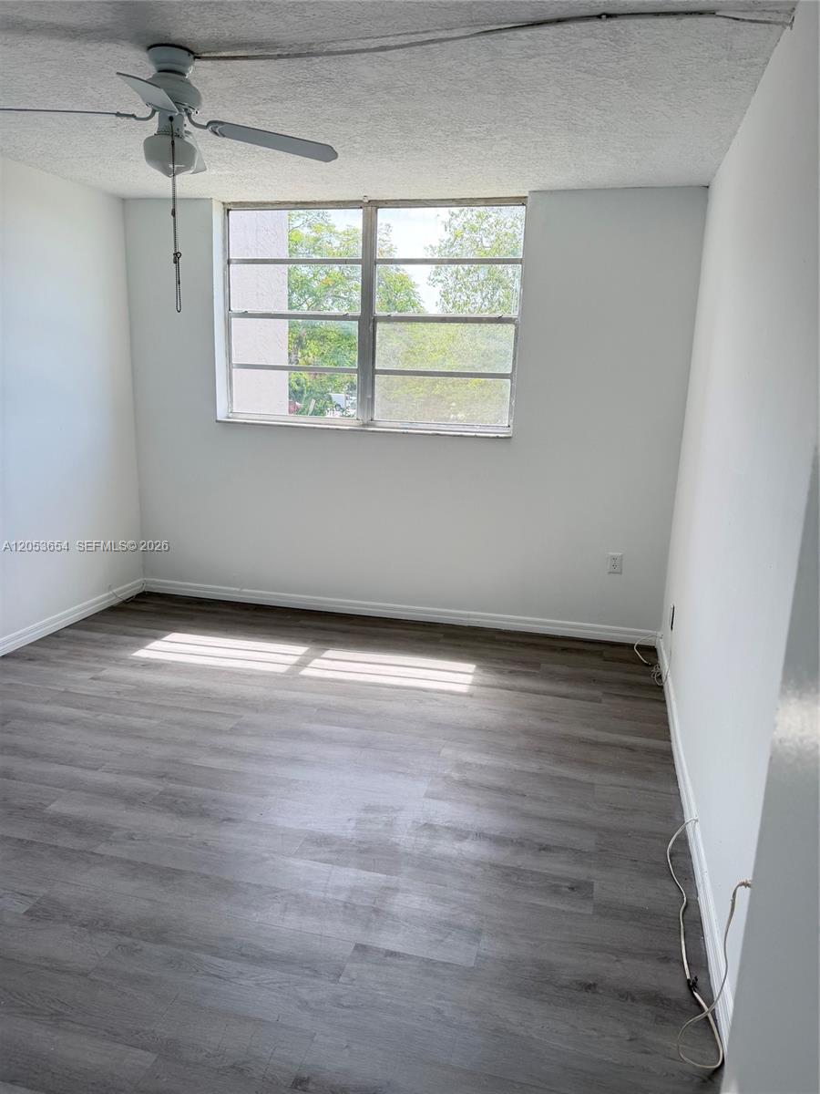 An empty bedroom features white walls, gray wood-look flooring, a ceiling fan, and a window — 14185 SW 87th St # 212A, Miami FL 33183, MIAMI, FL