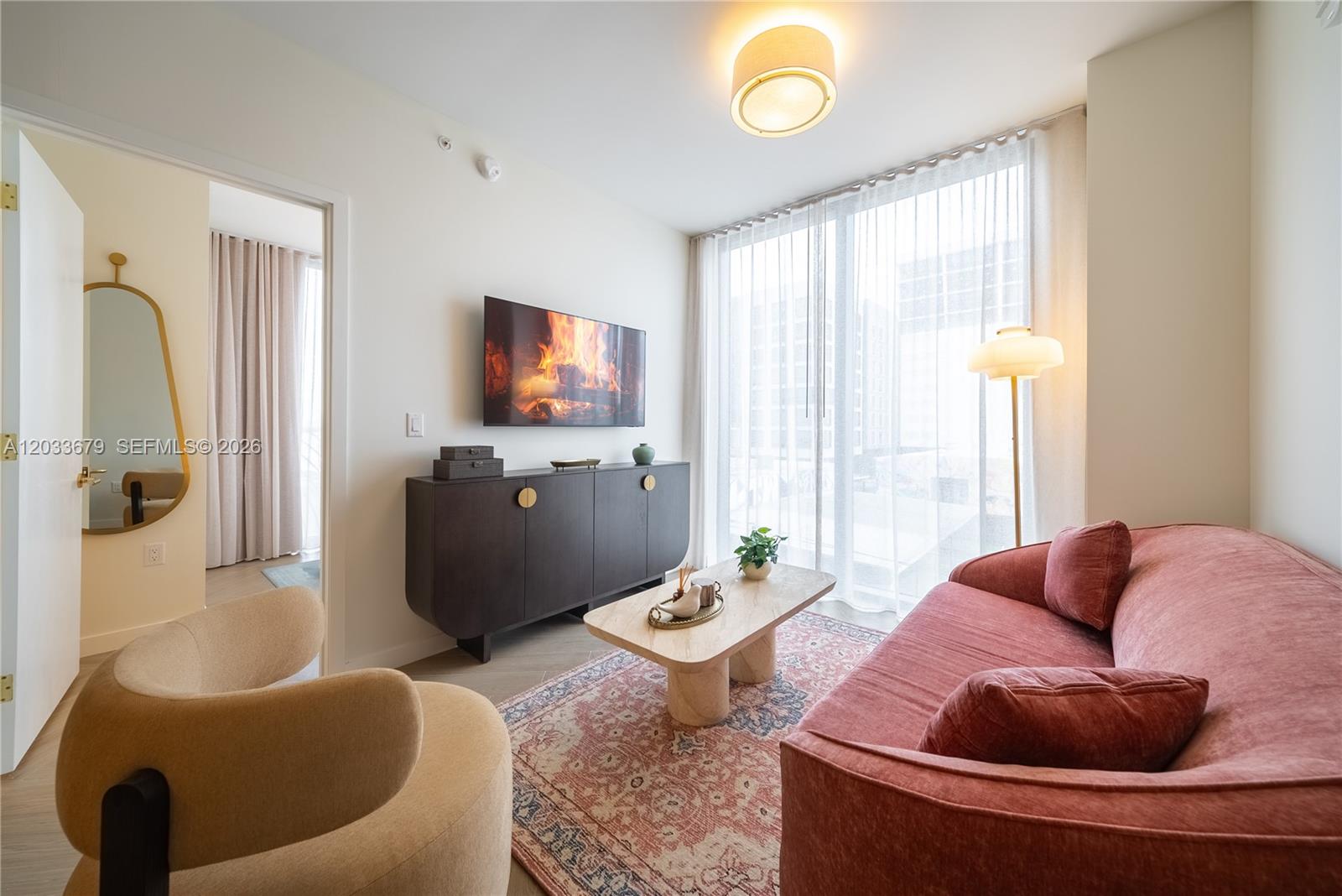 A living room features a pink curved sofa, a dark cabinet, and a patterned rug — 2700 NW 2nd Ave # 237, Miami FL 33127, MIAMI, FL